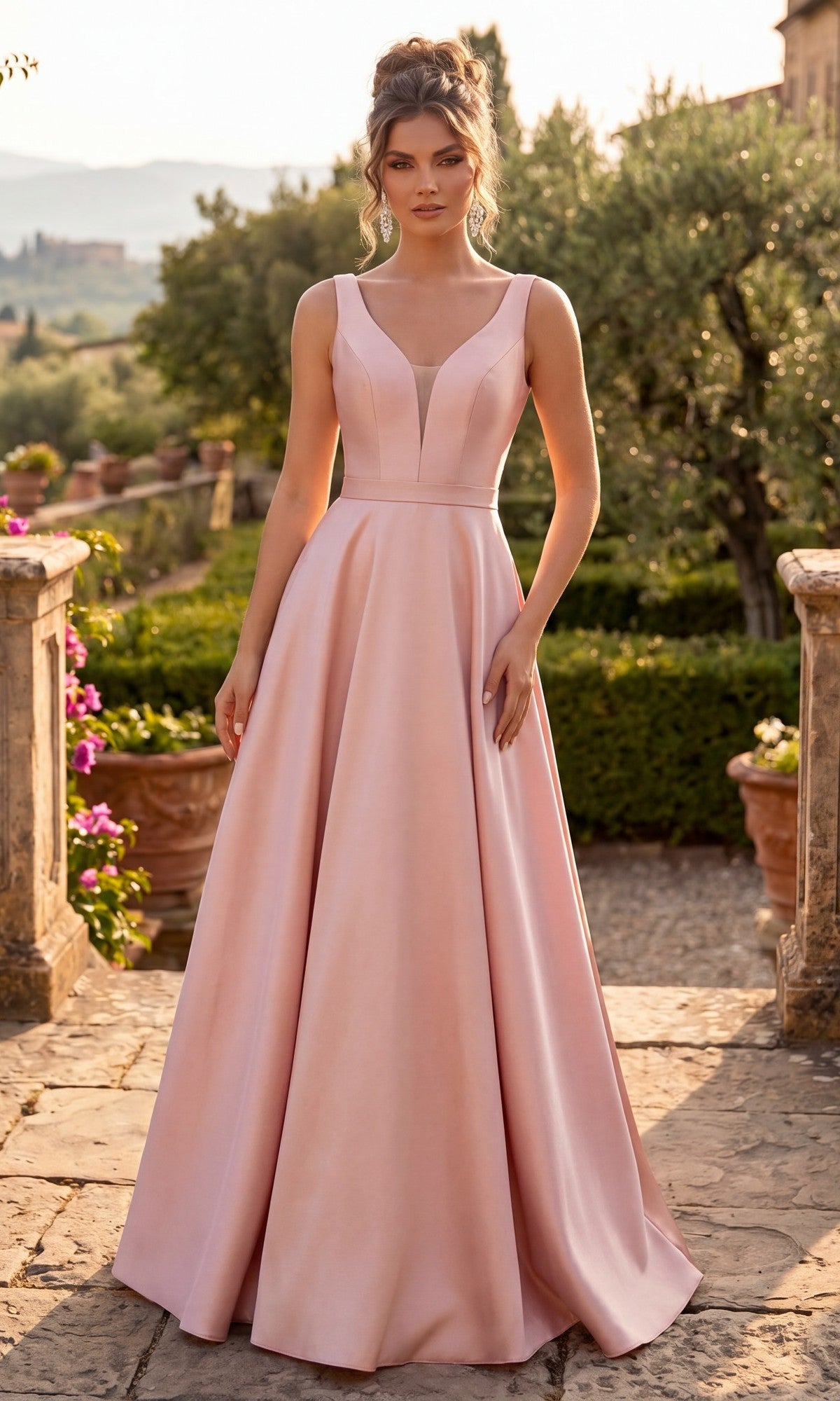 A woman in the Long Prom Dress: Chicas C9188, a sleeveless, floor-length gown in rose/pink with a fitted bodice and elegant A-line skirt, stands outdoors on a stone pathway surrounded by greenery and flowers, with a scenic landscape in the background.